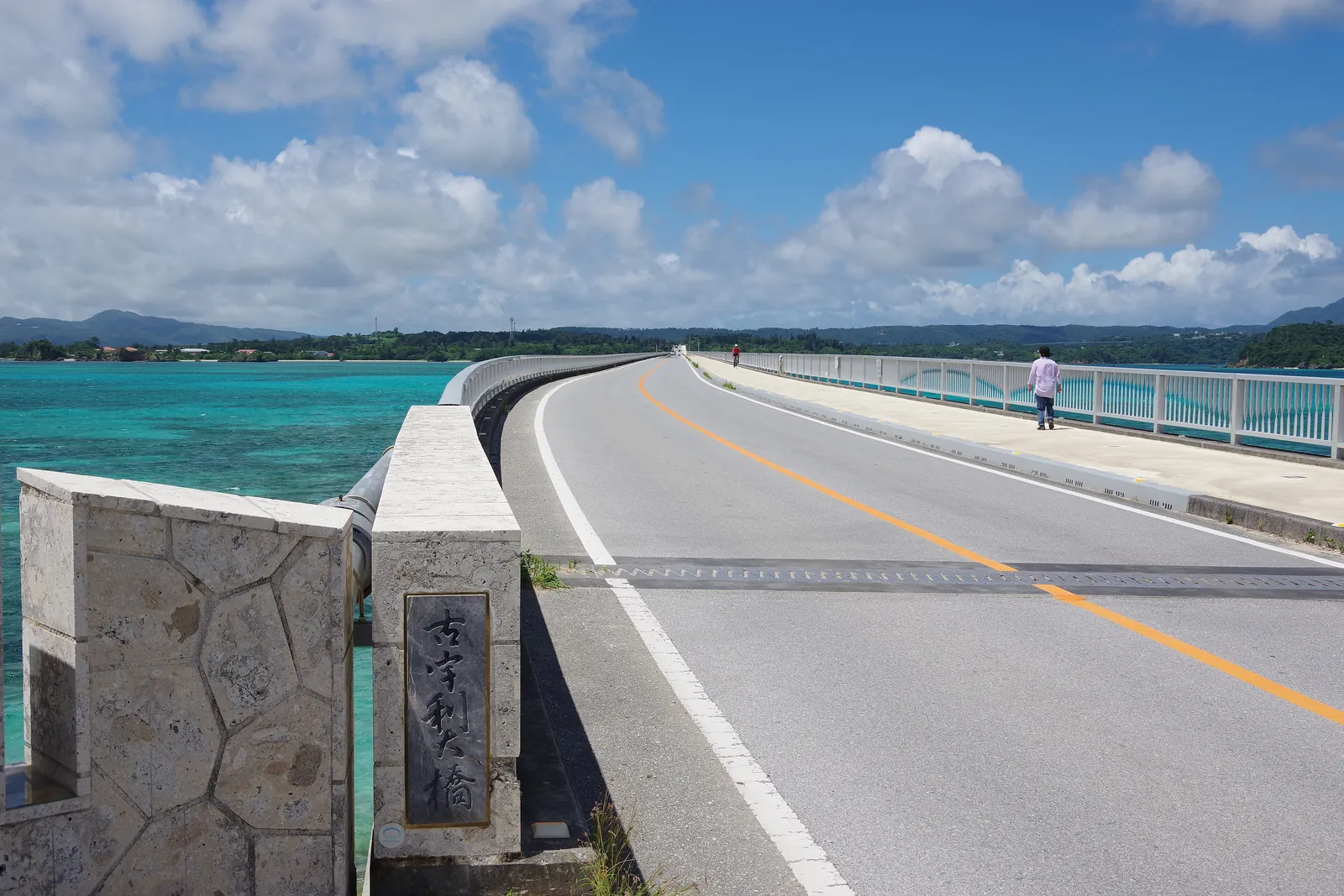 En vejbro over turkisblåt vand på en solrig dag med store hvide skyer; Kouri Bridge i det nordlige Okinawa, ikke parken